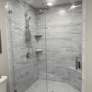 Glass doors on walk-in shower with grey tile and built-in seating. Beige bathroom