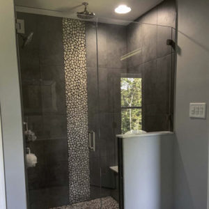 Glass shower door on dark gray walk-in shower with stripe of smaller tiles on center wall