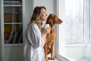 Happy woman drinking coffee and looking outside of large window