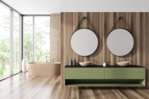 A modern bathroom with floor-to-ceiling windows, wood flooring, and a green vanity with circle mirrors